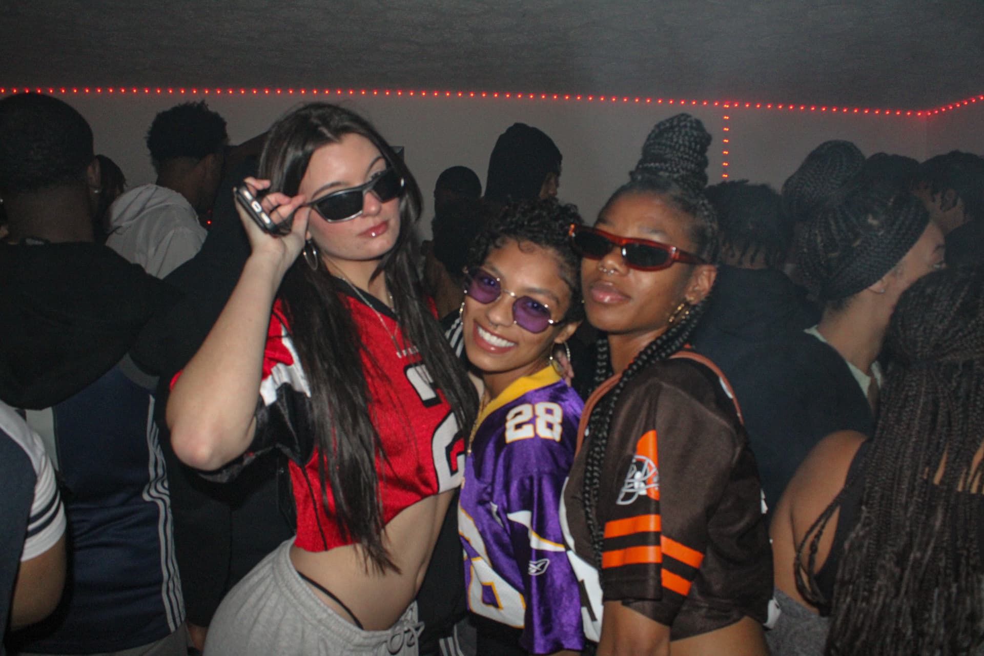 Three friends posing in sports jerseys at an indoor party